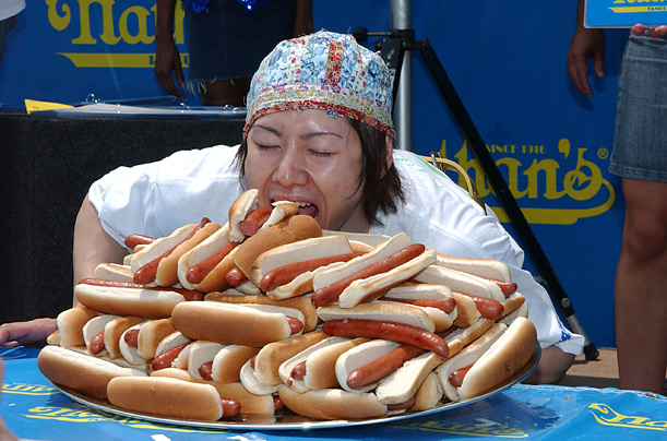 woman competitively eating pile of hot dogs