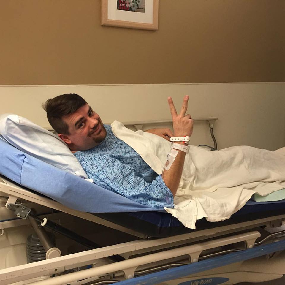 man laying on gurney giving the victory sign with his hands